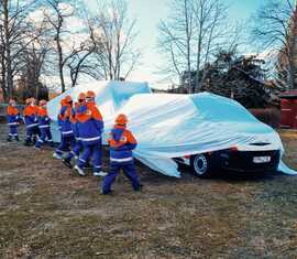 Mitglieder der Jugendfeuerwehren des Amtes Döbern-Land enthüllen ihr neues Mannchaftstransportfahrzeug mit Anhänger.